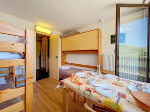 A compact room with bunk beds, a dining table set for two, and a view of a balcony. - Studio at the slopes with balcony (Les Menuires)