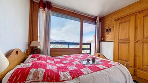 Ein Schlafzimmer mit einem großen Bett, einem Fenster mit Blick auf die Berge, Holzwänden und einer Heizung.
