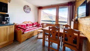 Ein gemütliches Zimmer mit einer Holzsofa, einem Esstisch mit Stühlen, einer Küchenzeile mit Mikrowelle und Kaffeemaschine sowie einem großen Fenster mit schöner Aussicht.