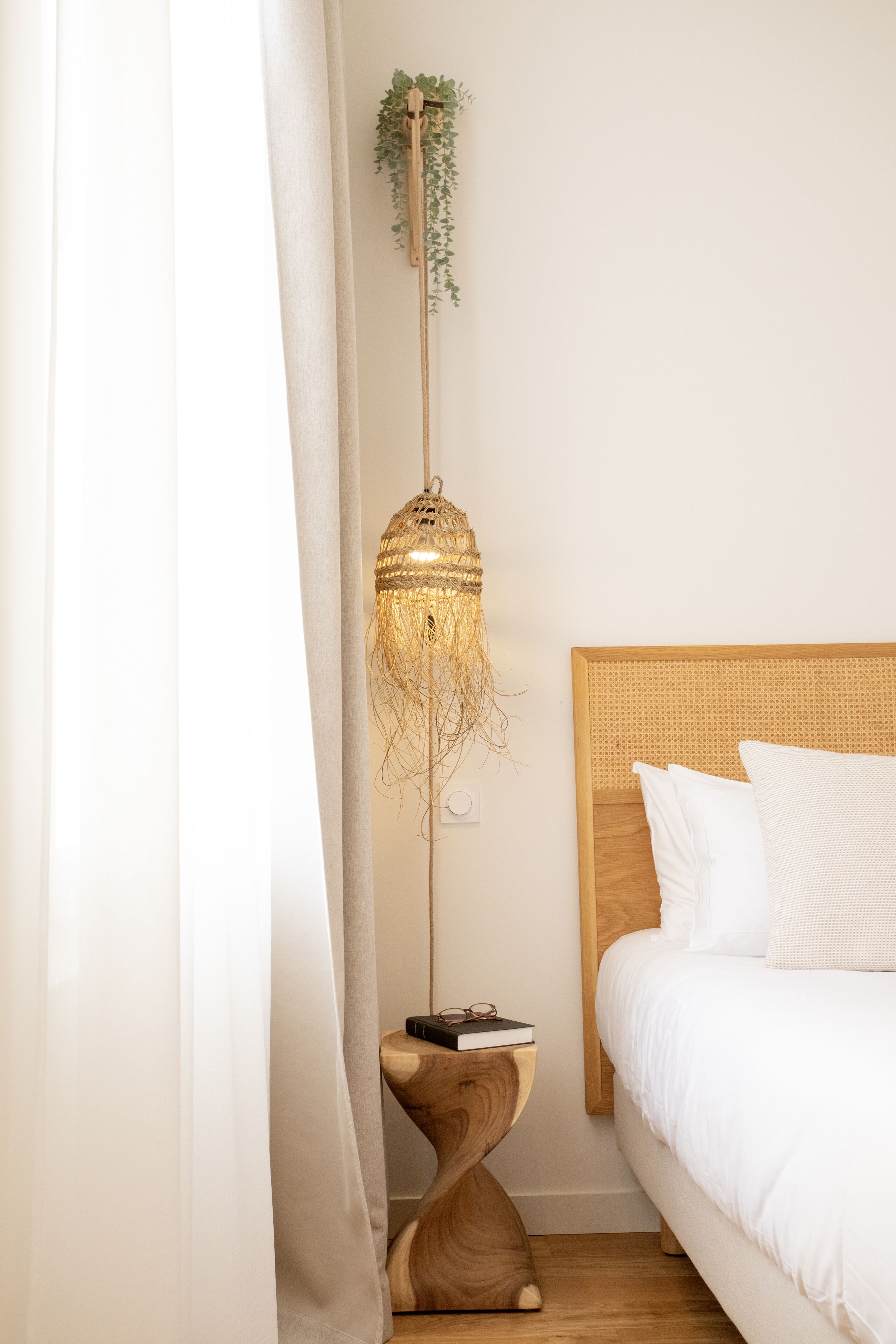 Een slaapkamer met een houten hoofdeinde, een nachtkastje met een plant erop en een hanglamp.