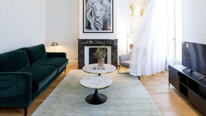 A modern living room with a dark green sofa, a round marble coffee table, a fireplace, and a large window with sheer curtains. - Les Clés Secrètes (Sète)