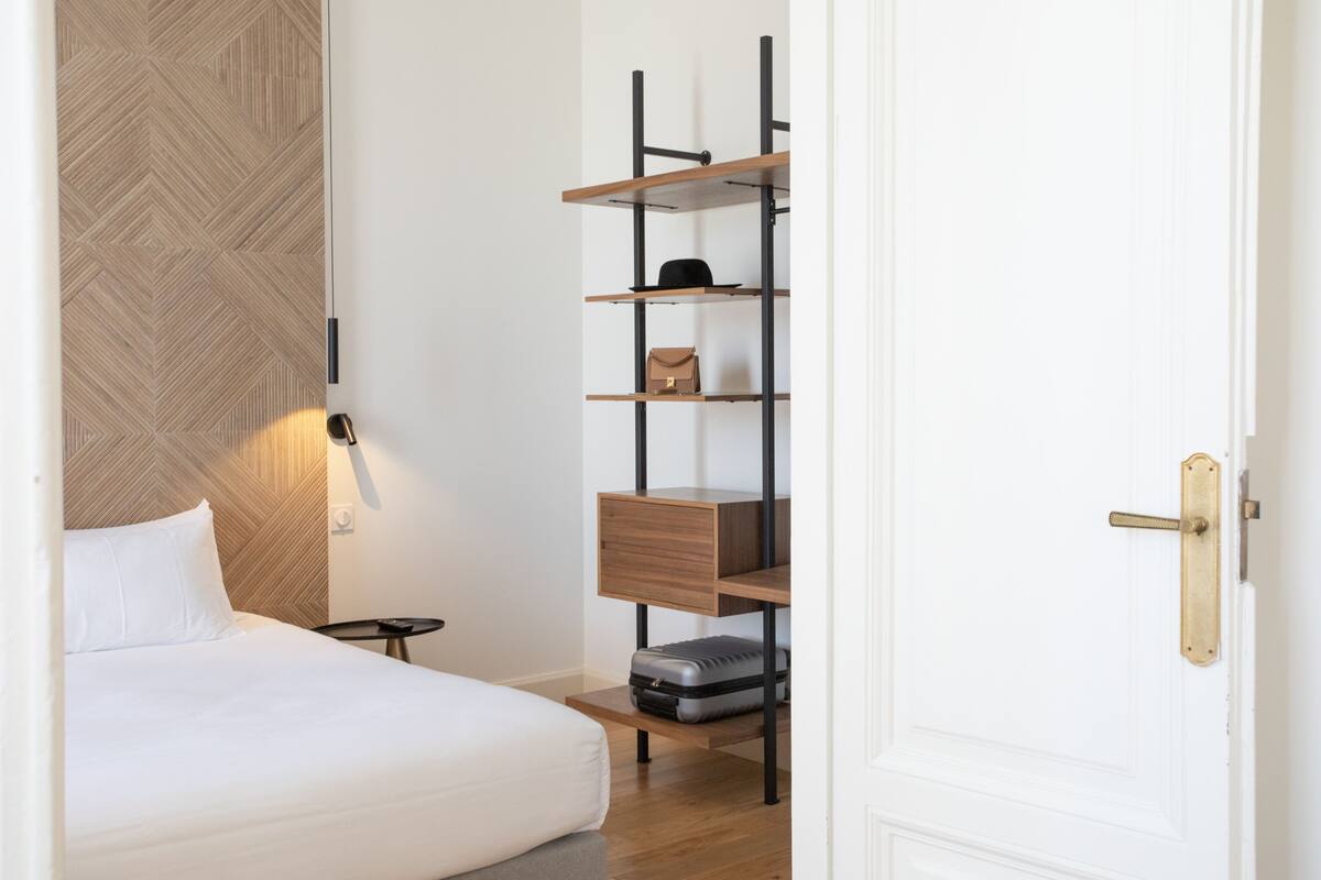 Habitación de hotel con una cama, cabecera de madera, estante con una maleta y una puerta.