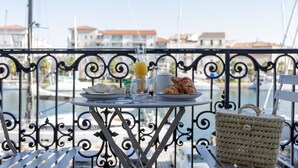 A balcony with a table set for breakfast, including croissants, a glass of orange juice, and a cup. A woven bag is also visible on the table. - Les Clés Secrètes (Sète)