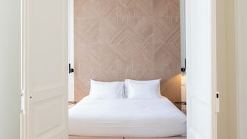 A bedroom with a bed, wooden herringbone-patterned headboard, white bedding, and a pair of shoes on the floor.