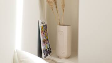 A white wall with a small shelf containing a white vase with pampas grass and a magazine.