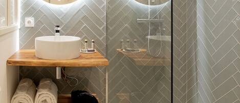 A modern bathroom with a glass-enclosed shower, a round mirror, and a wooden vanity with towels.