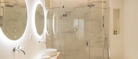 A modern bathroom with a large bathtub, a glass-enclosed shower, and three round mirrors.
