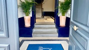 A hotel entrance with a blue mat reading "LES CLÉS SECRETES" and a staircase leading to the interior. - Les Clés Secrètes (Sète)