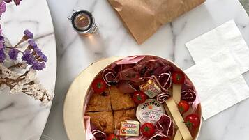Une table ronde avec un plateau en marbre, un plateau rond contenant des aliments, un sac en papier brun, une petite bouteille en verre et un arrangement floral décoratif.
