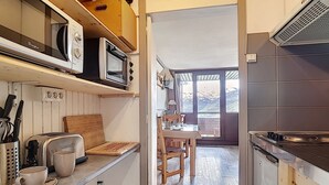 A compact kitchen with a microwave, toaster, and wooden counter. A dining area with a table and chairs is visible through an open door.