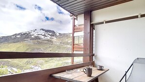 A balcony with a wooden table and chairs, overlooking a mountainous landscape.