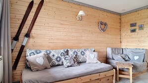A wooden interior with a sofa and a small table, a wall-mounted lamp, and a heart-shaped decoration.