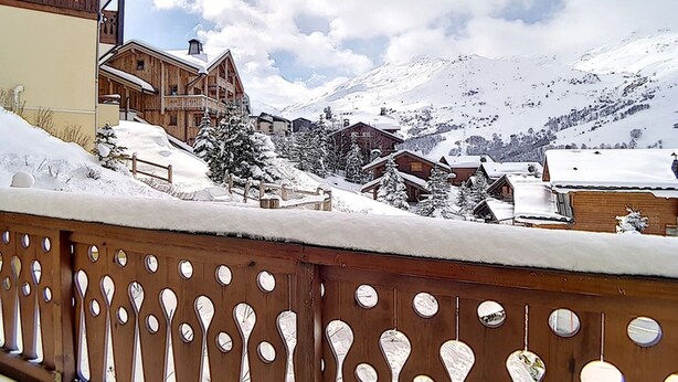 Una cabaña de madera con balcón que da a un pueblo de montaña cubierto de nieve.