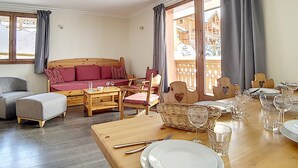 Una habitación acogedora con un sofá de madera, una mesa de comedor para cuatro personas y un balcón con barandilla de madera.