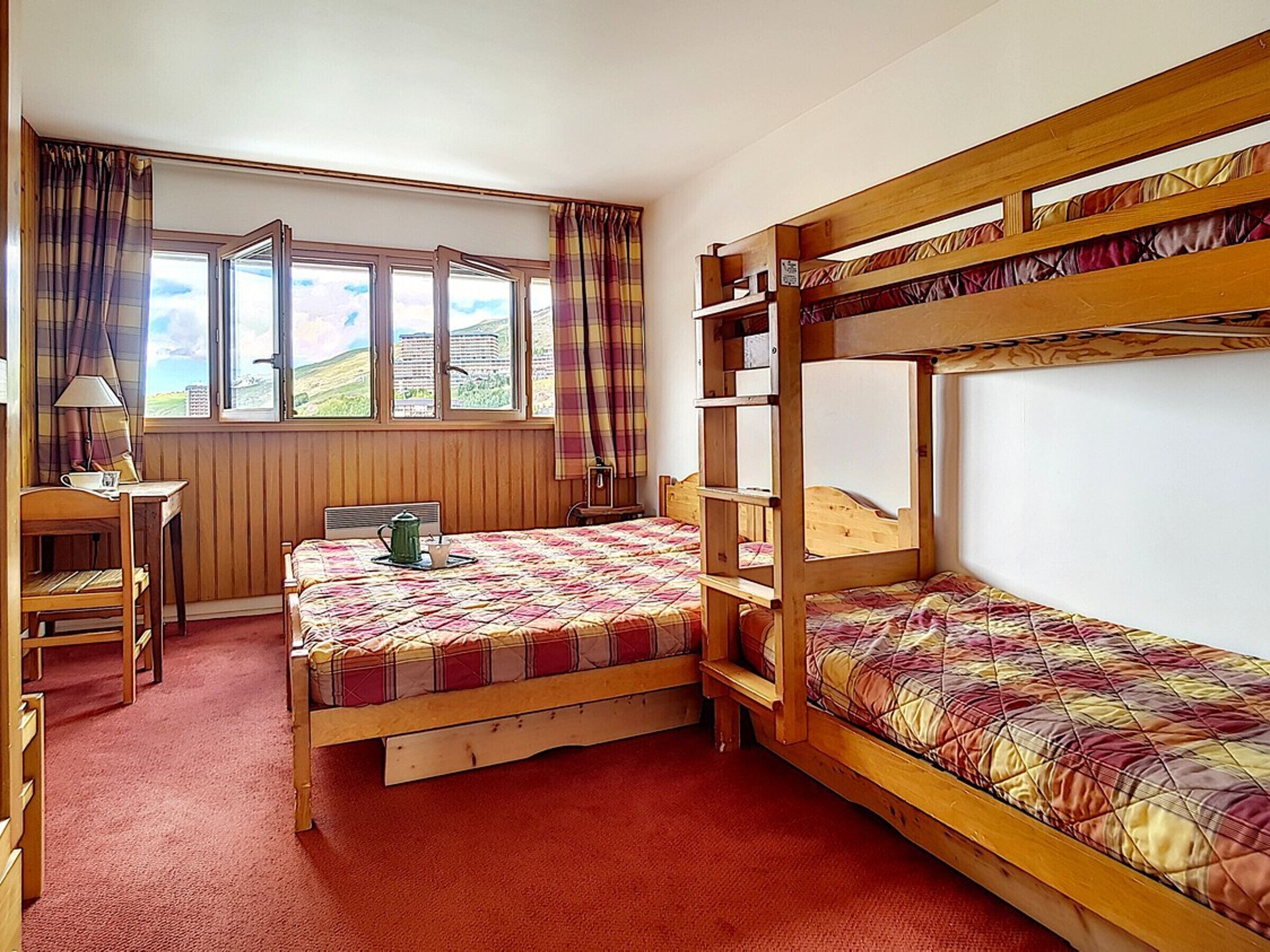 Une chambre avec deux lits superposés, un bureau, une chaise et une fenêtre avec des rideaux.