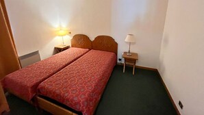 Una habitación pequeña con una cama individual, cabecera de madera, dos mesitas de noche y alfombra verde.