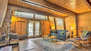 Een knus houten interieur met een stenen openhaard, houten wanden, een bank en een schommelstoel.