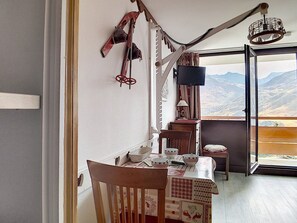 A dining area with a table set for two, a chair, a lamp, and a view of mountains through a large window. - Bright studio in center, balcony, 3 Gold flakes (Les Menuires)