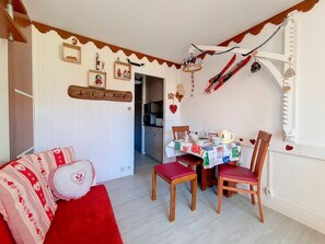 A cozy dining area with a table set for two, wooden chairs, and a red sofa with patterned cushions. - Bright studio in center, balcony, 3 Gold flakes (Les Menuires)
