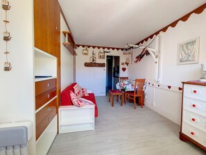 A cozy living room with a red sofa, wooden cabinets, and a dining area with a table and chairs. - Bright studio in center, balcony, 3 Gold flakes (Les Menuires)