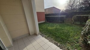 Un espace extérieur aménagé en patio, avec un sol carrelé, une petite pelouse et une clôture en bois.