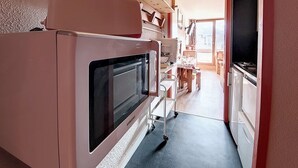 Una cuina compacta amb forn integrat, microones i zona de menjador petita amb taula i cadires.