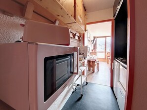 A compact kitchen with a built-in oven, a microwave, and a small dining area with a table and chairs. - Bright studio in center · South balcony · 4 guests (Les Menuires)