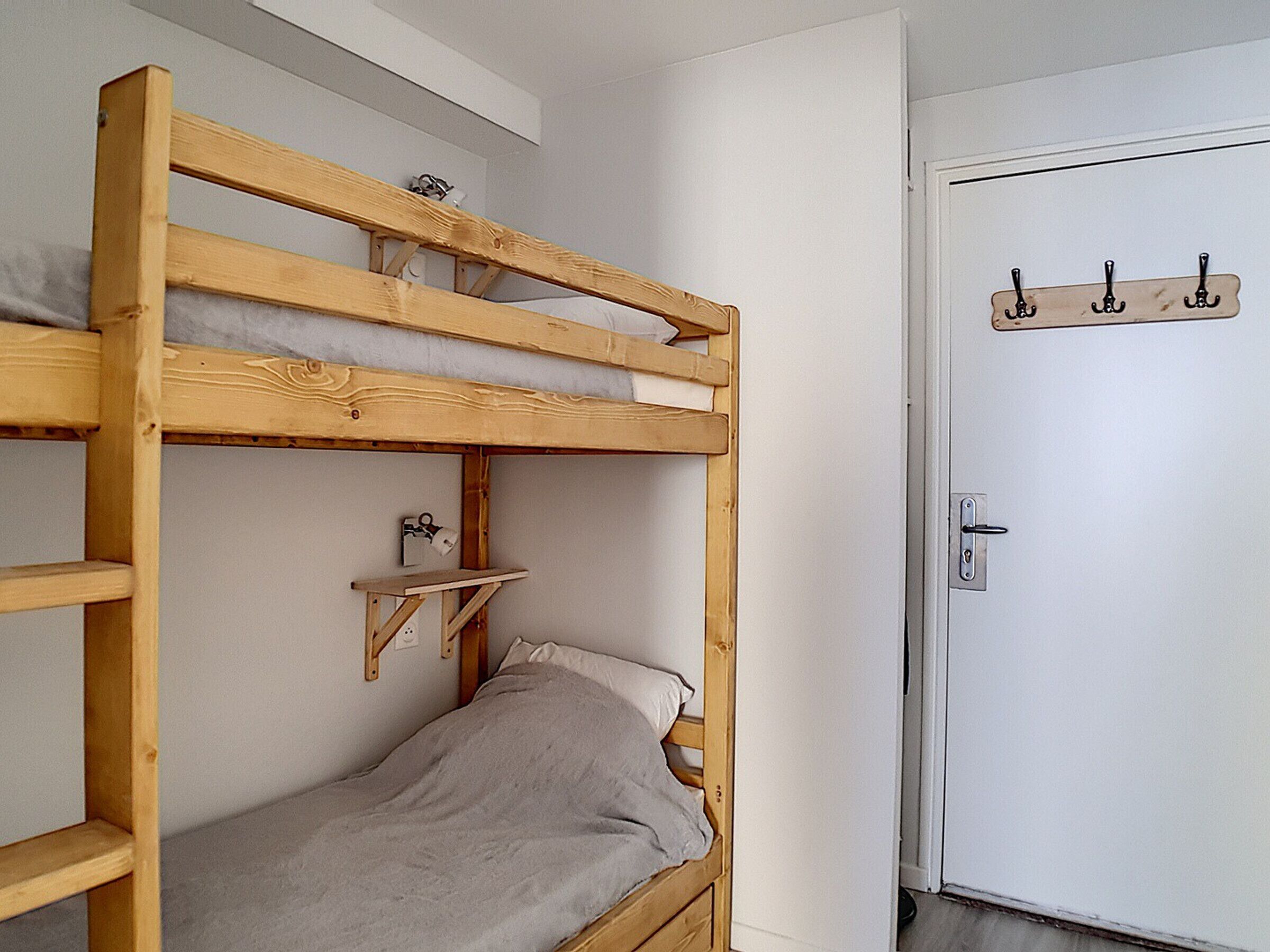 A bunk bed with a shelf and a door with a coat hook.
