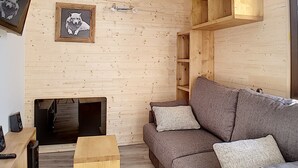 Uma sala de estar acolhedora com parede de madeira, um sofá cinzento e um quadro com a imagem de um cão.