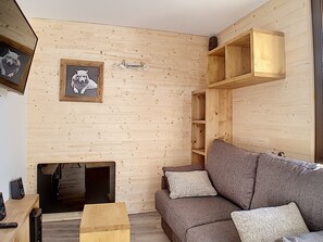 A cozy living room with a wooden wall, a grey sofa, and a framed picture of a dog.