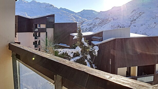 Um edifício moderno com varanda com vista para uma paisagem montanhosa coberta de neve.