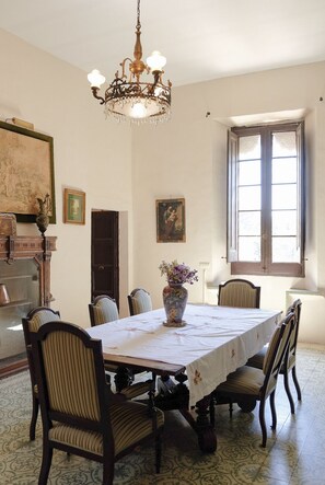 A dining room with a large table, chairs, a chandelier, and artwork on the walls.