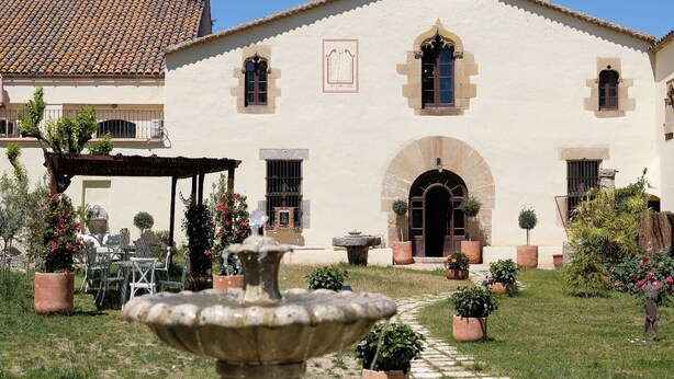 Un edificio tradizionale con tetto in tegole, un arco centrale e una fontana in primo piano.