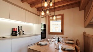 Una cocina moderna con armarios blancos, una mesa de comedor de madera para cuatro personas y un horno empotrado.