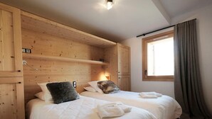 Un dormitorio con dos camas, paneles de madera, una ventana con cortinas y una lámpara de noche.