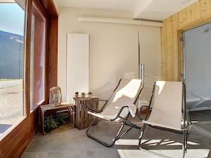 Ein modernes Zimmer mit zwei weißen Stühlen, einem kleinen Tisch mit Pflanzen und Blick ins Freie.