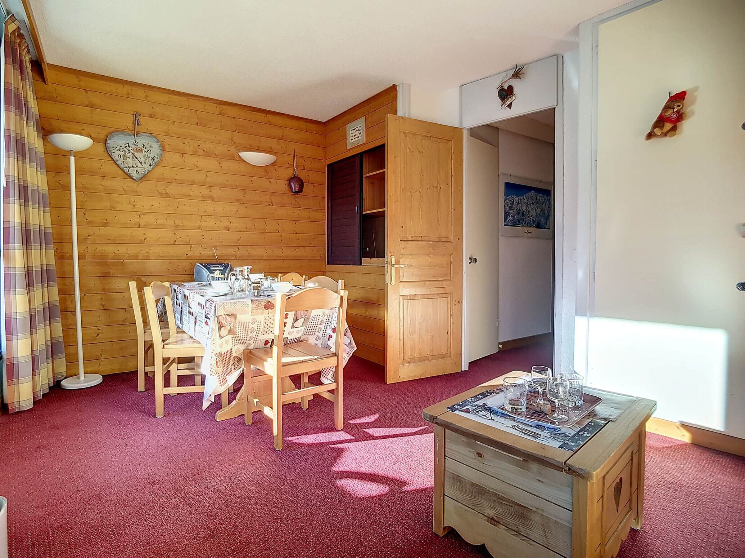 A cozy room with wooden walls, a dining table set with chairs, a small wooden cabinet, and a red carpet.