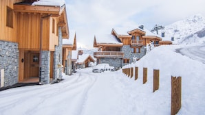 En snötäckt fjällstuga med träarkitektur, stenmurar och en skidlift i bakgrunden.