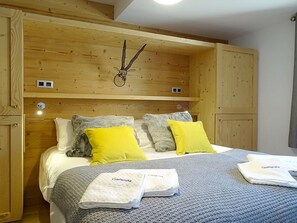 A wooden-framed bedroom with a bed, pillows, and towels.
