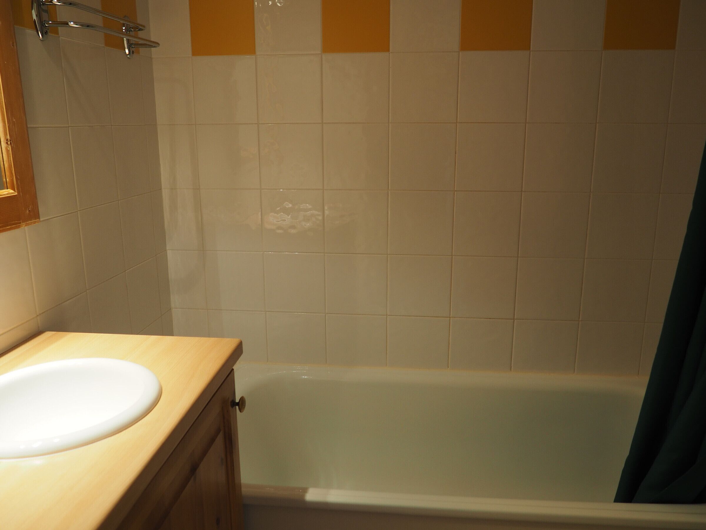 Een badkamer met een witte wastafel, een houten opbergmeubel en een bad.