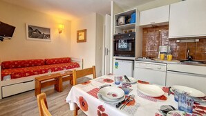 A compact living space with a dining area, kitchenette, and a red sofa. - Cozy studio at the foot of the slopes, balcony, pets allowed (Les Menuires)
