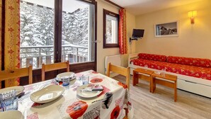 A cozy room with a dining table set for two, a sofa, and a TV mounted on the wall. - Cozy studio at the foot of the slopes, balcony, pets allowed (Les Menuires)