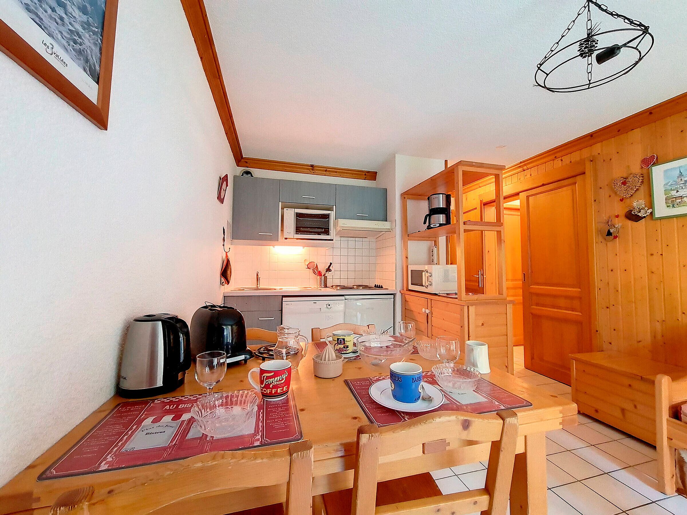 A compact kitchen with modern appliances, a dining table set for two, and a wooden cabinet with a microwave.