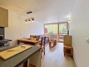 Eine moderne Küche mit Essbereich, Holzmöbeln und einem großen Fenster mit Blick ins Freie.