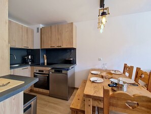 A compact kitchen with modern appliances, a dining table set for two, and a pendant light fixture.