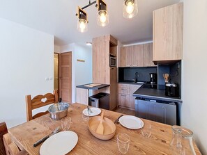 A modern kitchen with wooden cabinets, a dining table set with plates, glasses, and cutlery, and a coffee maker.