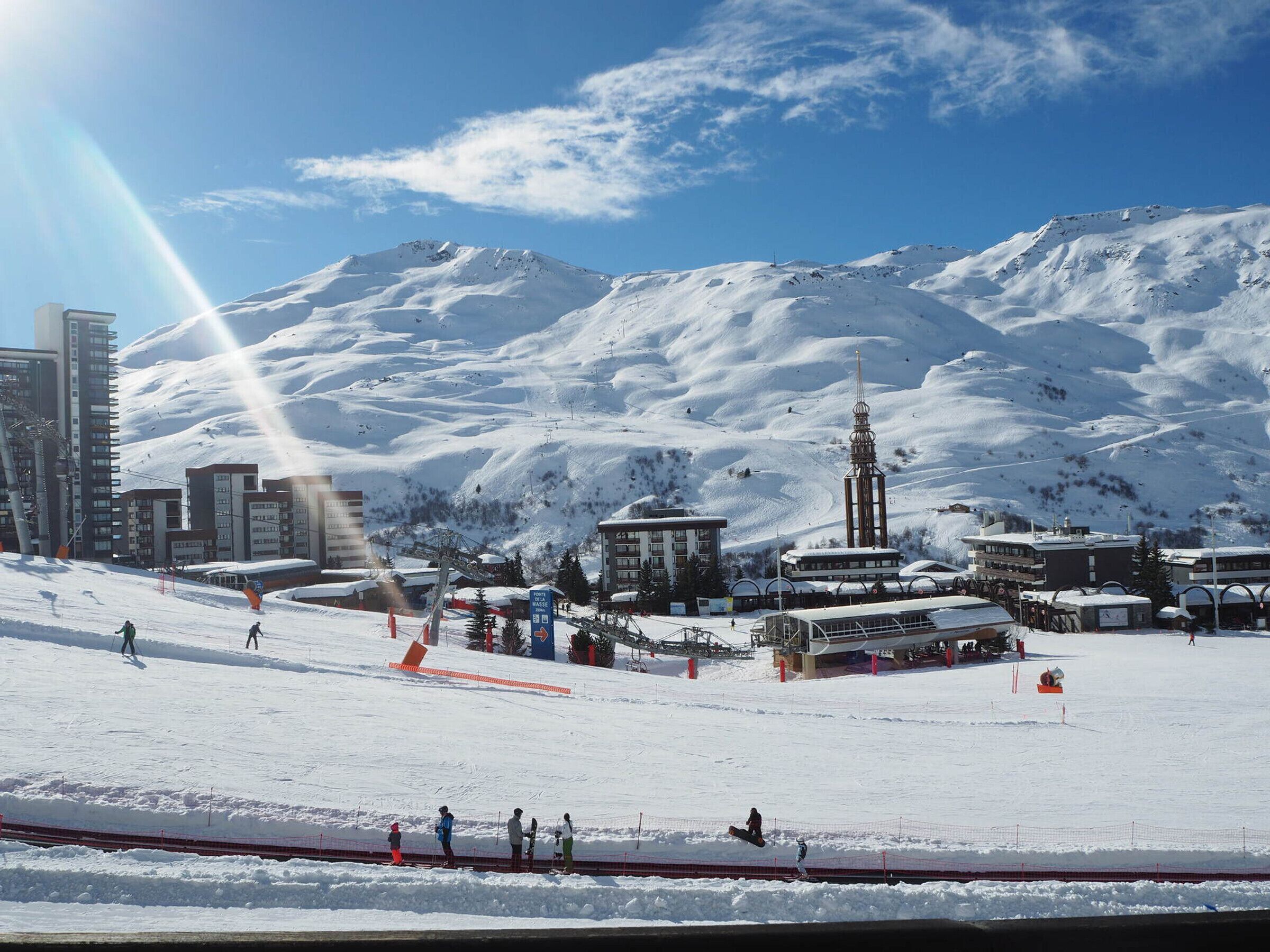 A snowy ski resort with a ski lift, buildings, and a mountain backdrop.