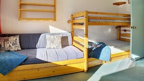 Et værelse med køjeseng, en sofa med mønstrede puder, en lille hylde med en rød vase og en dør.
