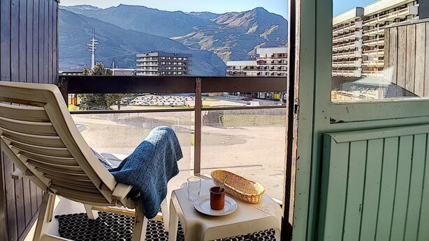 En balkon med liggestol og bord, med udsigt over et bjerglandskab og et vandområde.