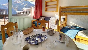 Et hyggeligt værelse med køjeseng, et bord dækket med tallerken, glas og kande, samt et vindue med udsigt til et bjerglandskab.